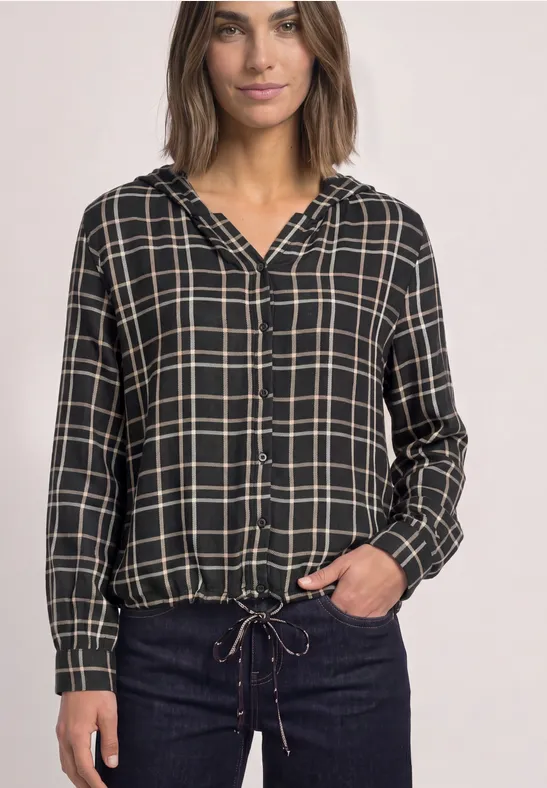 Frau in schwarzem kariertem Kapuzenhemd mit Tunnelzug am Saum und dunkler Jeans.