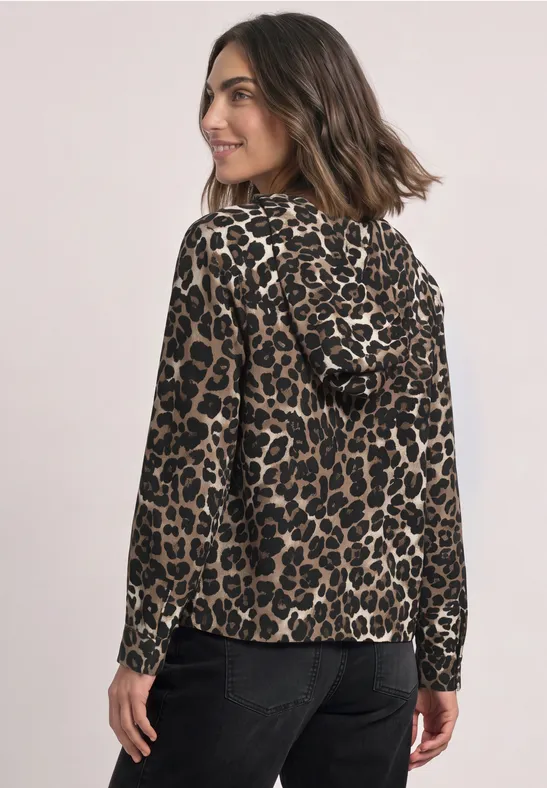Frau im Leoparden-Kapuzenshirt, langärmelig, blickt über die Schulter, kombiniert mit schwarzer Hose.