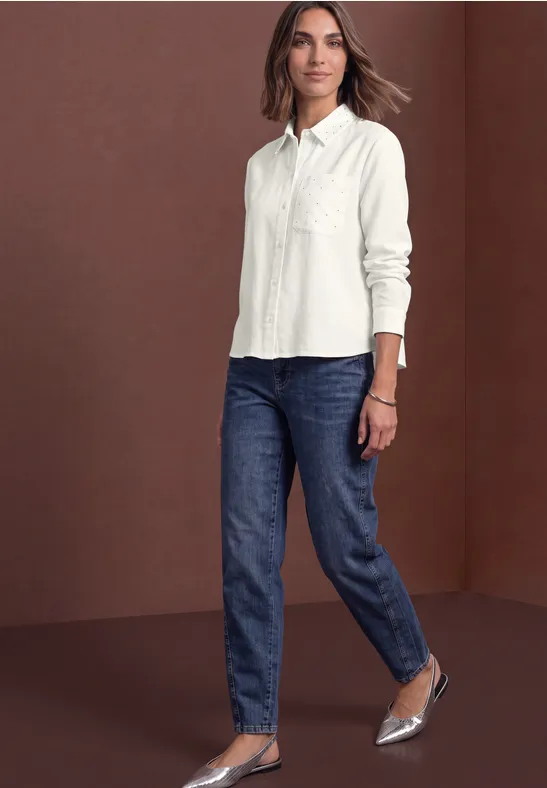 Frau trägt weiße Bluse, dunkelblaue Jeans und silberne High Heels, geht selbstbewusst vorwärts.