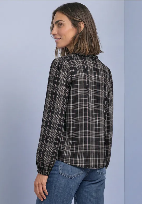 Eine Frau trägt eine karierte Bluse und Jeans und blickt seitlich über die Schulter.