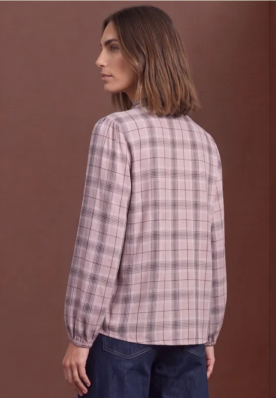 Frau von hinten in rosa kariertem Langarmhemd und Jeans vor braunem Hintergrund.