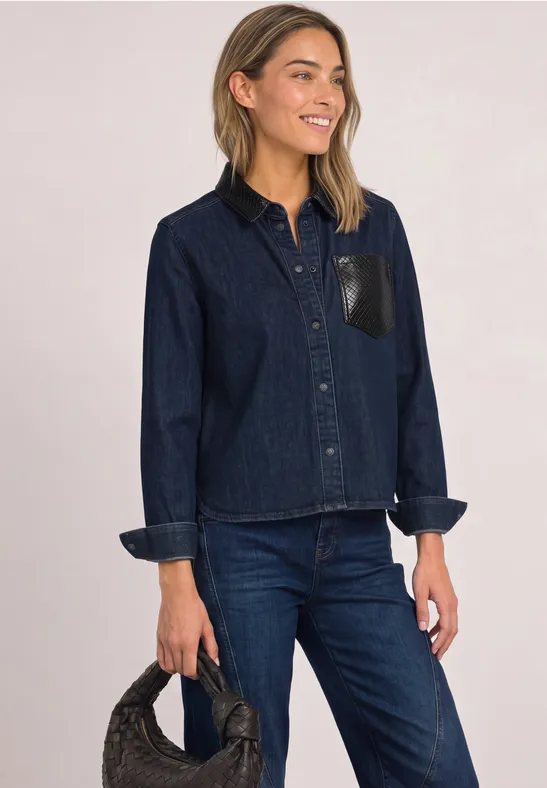 Frau in dunkelblauer Jeansjacke und Hose, hält schwarze Handtasche.
