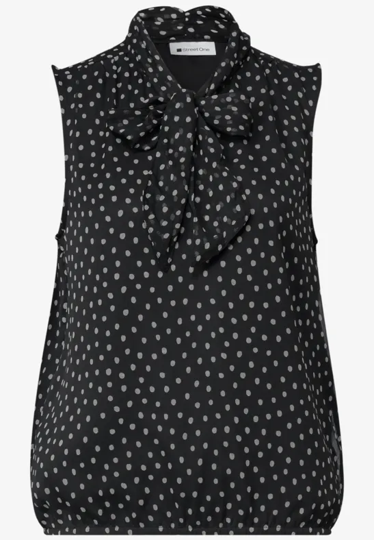 Ärmellose schwarze Bluse mit weißen Punkten und gebundenem Schleifenkragen.