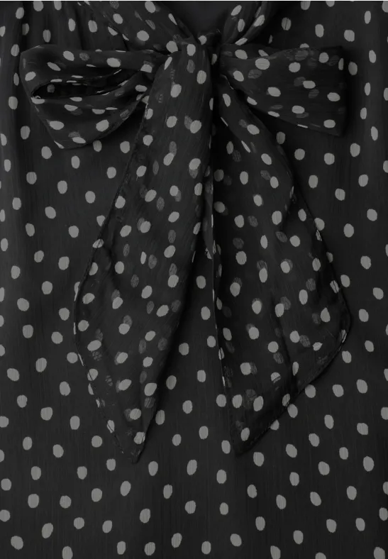 Schwarze Bluse mit weißen Polka-Dots und Schleifenbinder am Ausschnitt.