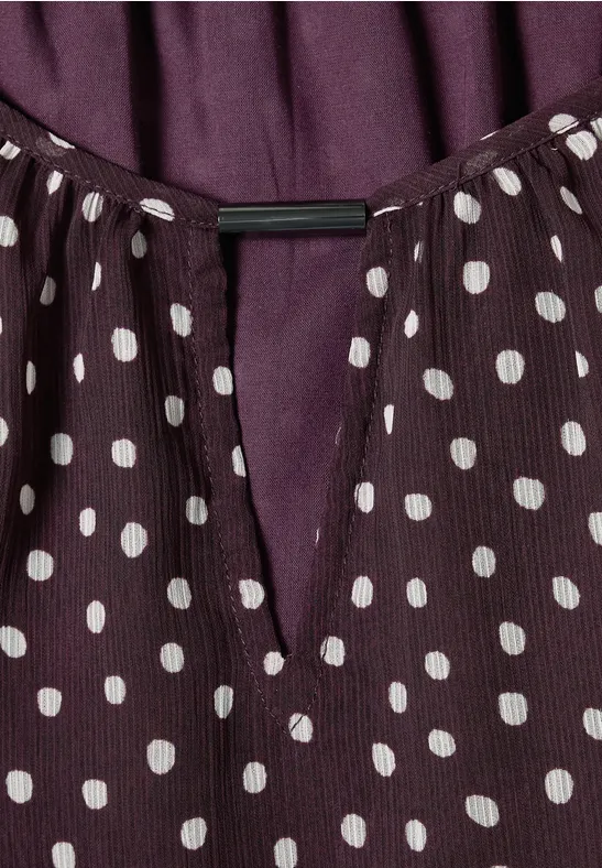 Violette Bluse mit weißen Polka Dots und V-förmigem Ausschnitt.