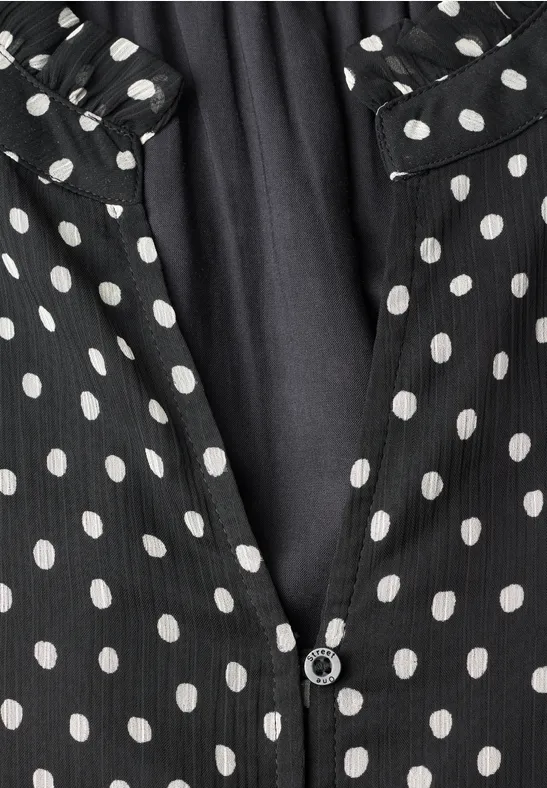 Schwarzer Stoff mit weißen Polka-Dots, mittig teilbar mit Knopf, gekräuselter Kragen.