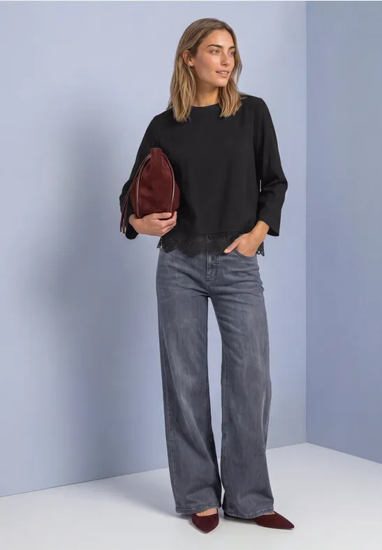 Frau trägt schwarze Bluse, weite graue Jeans, weinrote Tasche und spitze Schuhe.