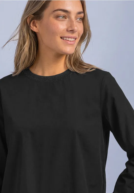 Eine lächelnde junge Frau in schwarzem Langarmshirt blickt seitlich in die Ferne.