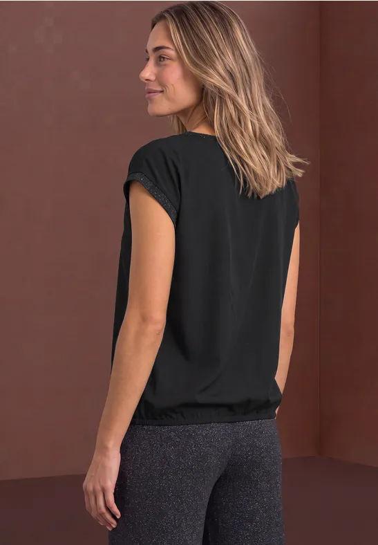 Damen-Sportoutfit: schwarzes T-Shirt, graue Leggings, seitlicher Blick auf braunem Hintergrund.