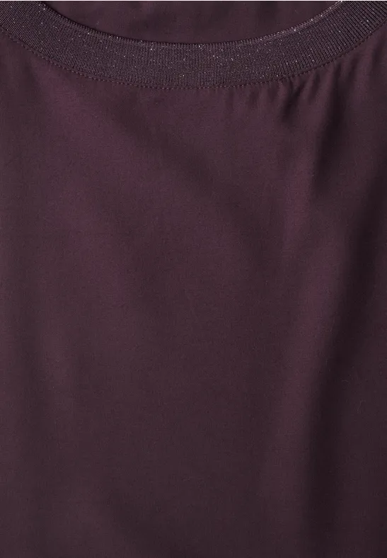 Gros plan sur l’encolure d’un t-shirt couleur baie, en tissu fin légèrement brillant.