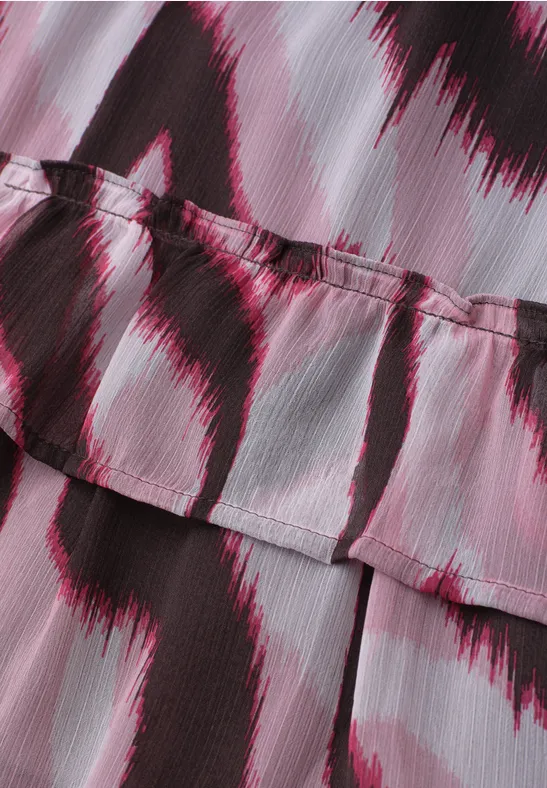 Gros plan d'un tissu rose à volants superposés, motif abstrait de coups de pinceau noirs.