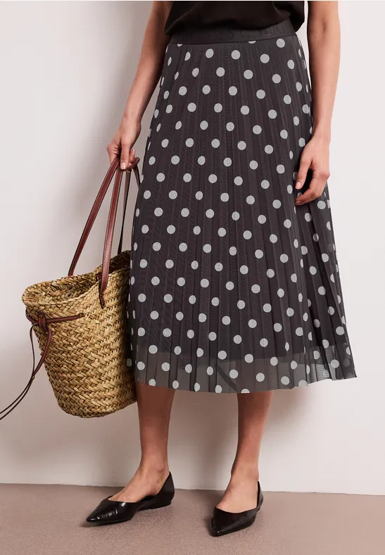 Jupe midi noire à pois blancs, ballerines noires et panier en osier tressé.