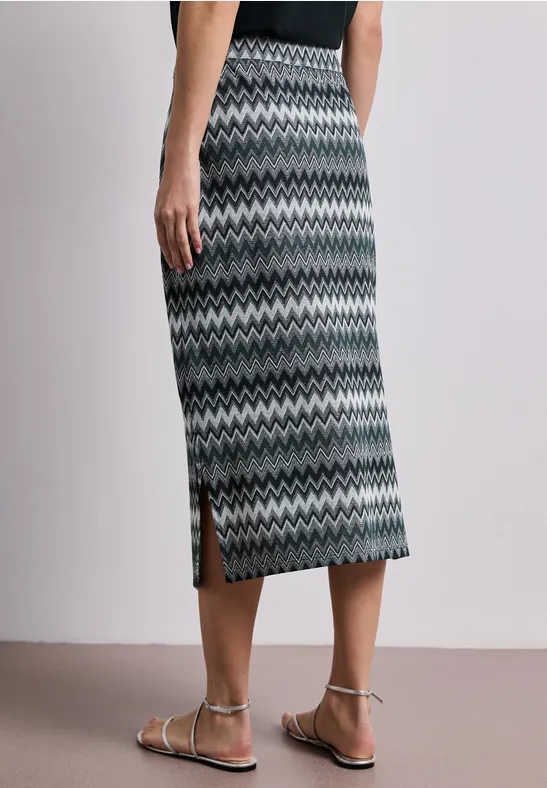 Strakke midirok met grijs zigzagpatroon en zijsplit, gecombineerd met een zwart topje en platte sandalen.