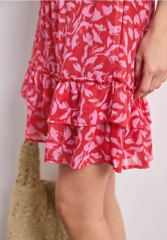 Roter Stufenrock mit rosa Blattmuster und Rüschen, Knielänge, daneben eine Basttasche.