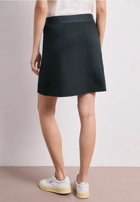 Frau von hinten in schwarzem Minirock und weißen Sneakern vor neutralem Hintergrund