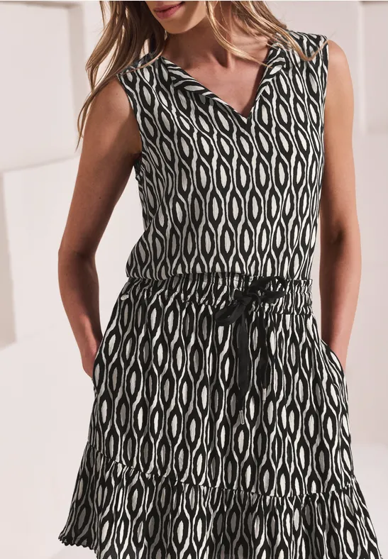 Mouwloze zomerjurk met zwart-witte etnoprint, V-hals, tailleceintuur en zakken.