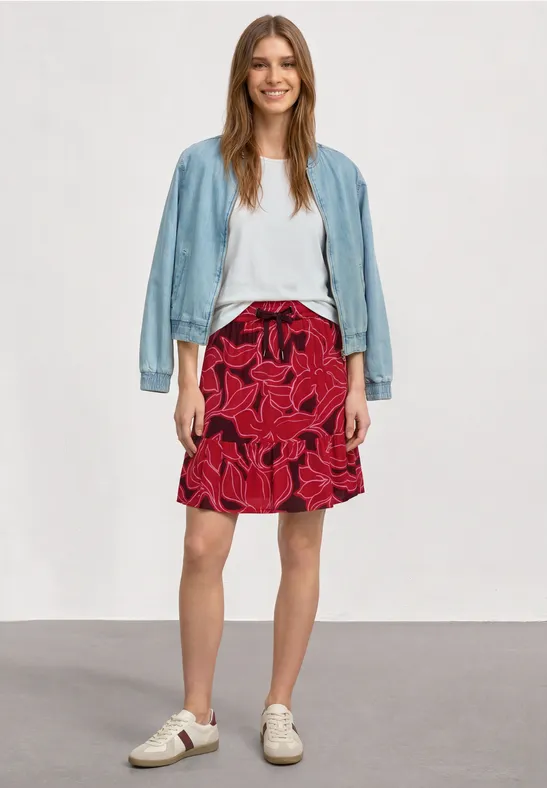 Frau trägt weißes Top, roten Blumenrock, hellblaue Jeansjacke und weiße Sneaker.