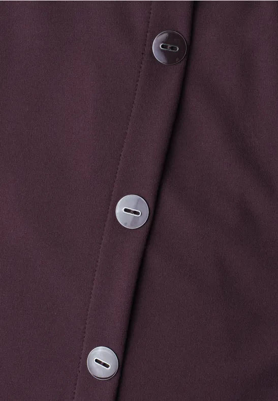 Nahaufnahme eines dunkelvioletten Kleidungsstücks mit drei silbernen Knöpfen.