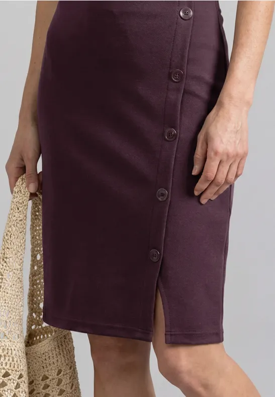 Midi-Bleistiftrock in Aubergine mit seitlicher Knopfleiste und Schlitz, kombiniert mit einer gehäkelten Netz-Tasche.