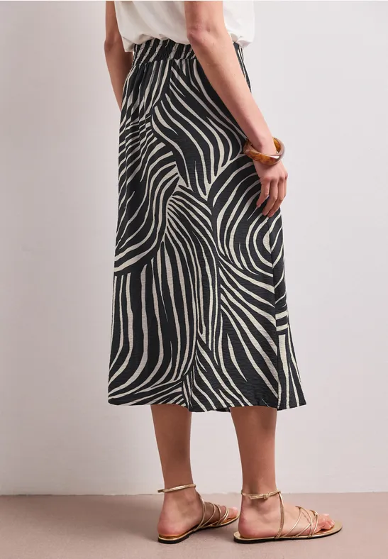 Vrouw van achteren in een zwart-wit zebrapatroon midirok met beige sandalen voor een neutrale muur.