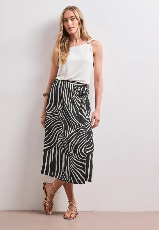 Vrouw met wit topje en zwart-witte midirok voor een witte muur