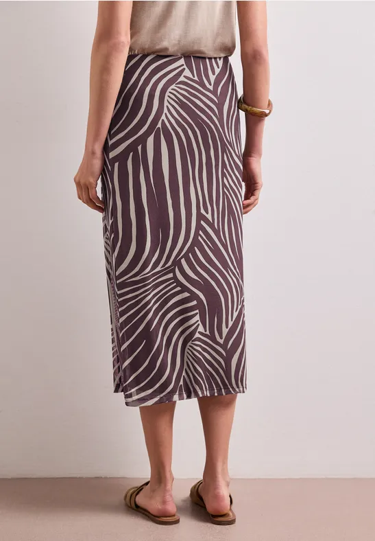 Vrouw van achteren in een midi-rok met bruin-beige zebraprint en platte sandalen.