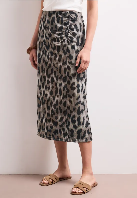 Vrouw draagt een midirok in luipaardprint en gouden sandalen.
