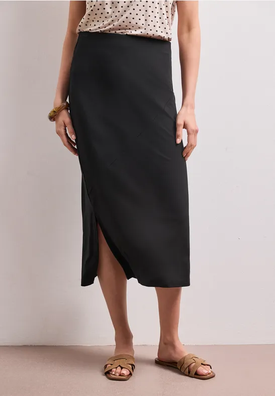 Zwarte midirok met zijsplit, gecombineerd met platte sandalen.