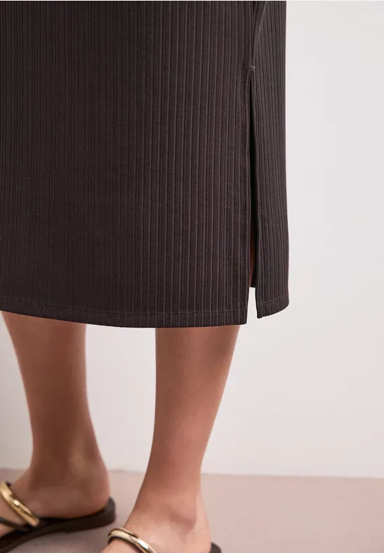 Iemand draagt een zwarte geribbelde midirok met een split en gouden sandalen.