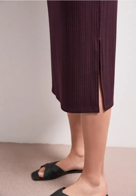 Zwarte sandalen met geknoopte bandjes, bordeaux geribde midijurk met zijsplit op beige achtergrond.