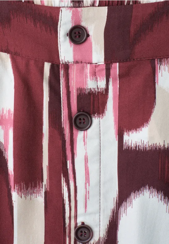Detail eines Hemds mit rot-weißem Pinselstrichmuster und drei dunklen Knöpfen.