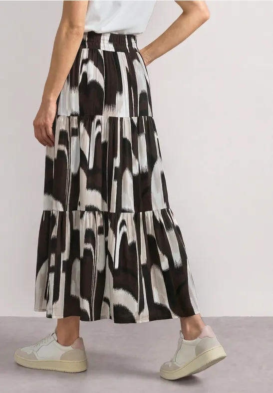 Zwart-witte gelaagde maxi-rok met abstract patroon, gecombineerd met witte sneakers.