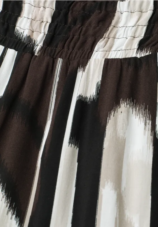 Close-up van een stof met elastische taille en abstract penseelstrepenpatroon in zwart, wit en beige.