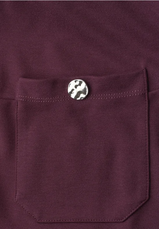 Bordeauxroter Stoff mit aufgesetzter Tasche und silbernem Knopf.