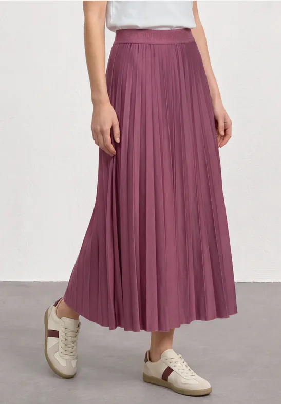 Une personne porte une jupe plissée longue couleur prune avec des baskets blanches.