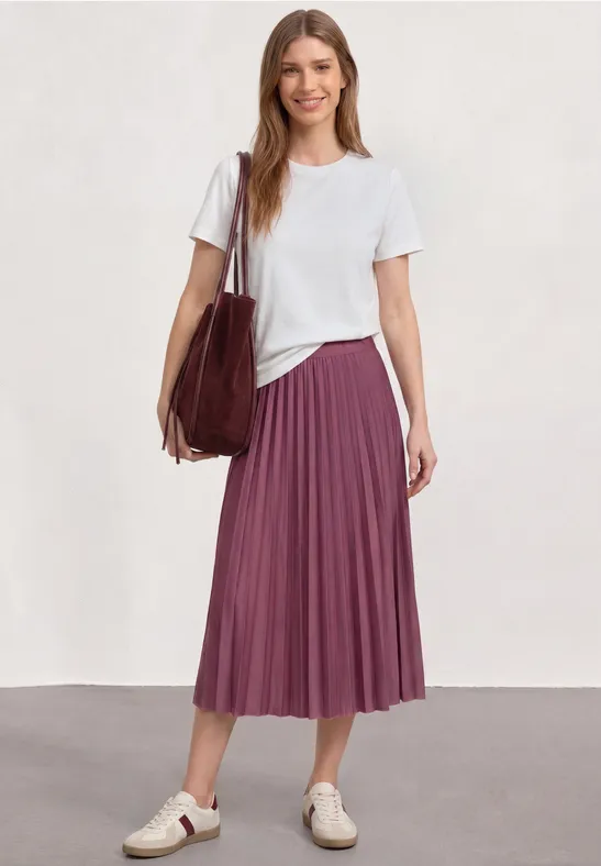 Femme en T-shirt blanc, jupe midi plissée violette, baskets blanches et grand sac.