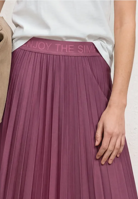 Une jupe mi-longue plissée prune avec taille élastique 'ENJOY THE SIMPL...' et un haut blanc.