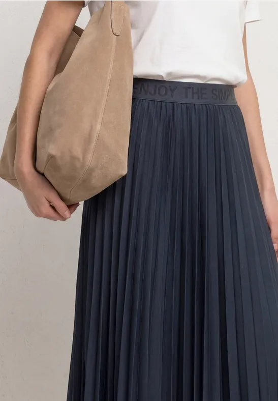 Frau mit weißem T-Shirt, dunkelblauem Plisseerock und beige Umhängetasche.