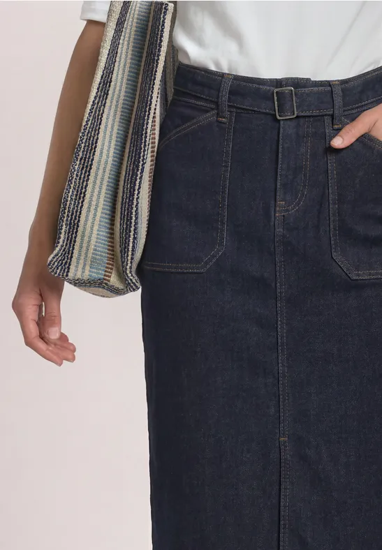 Frau trägt dunklen Jeans-Midirock mit aufgesetzten Taschen und Gürtel, kombiniert mit T-Shirt und gestreifter Tasche.
