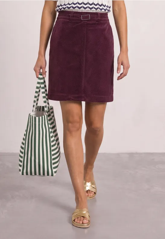 Frau trägt kurzen lila Cord-Rock, gestreifte Tasche und goldene Sandalen.