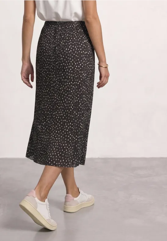 Frau von hinten in weißem Top, schwarzem Midirock mit dezentem Muster und weißen Plateau-Sneakern.
