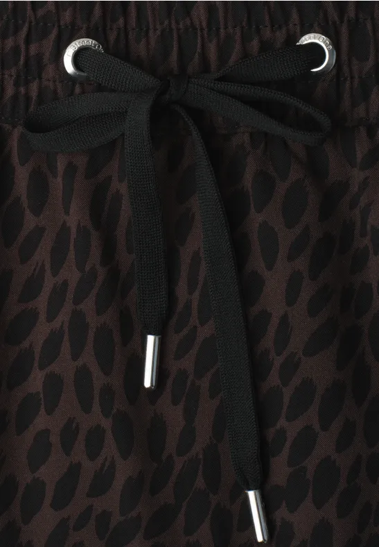 Gros plan sur un cordon noir à embouts métalliques sur un tissu marron à motifs.