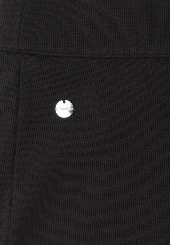 Gros plan sur un tissu noir côtelé avec un petit emblème métallique rond.