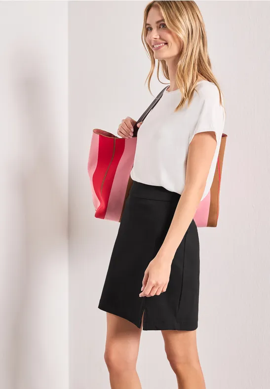 Femme en t-shirt blanc et jupe noire portant un sac rouge à l'épaule.