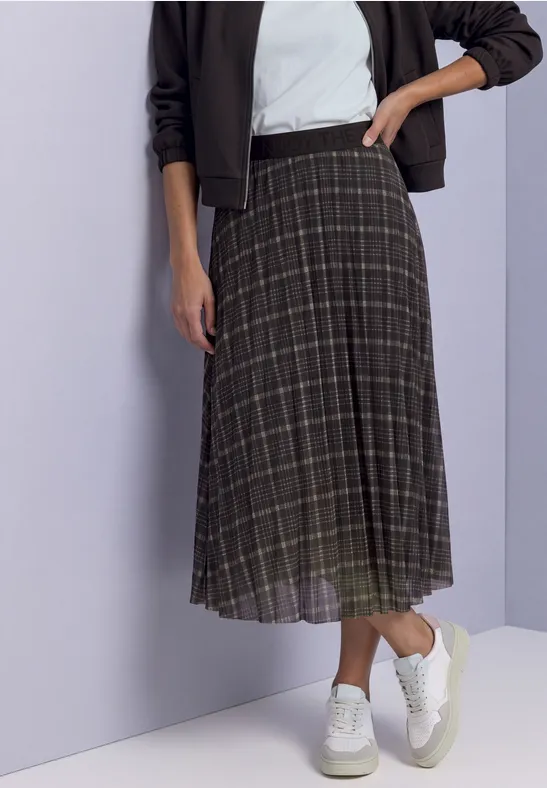 Vrouw in geruite midirok en witte sneakers, hand in heup.