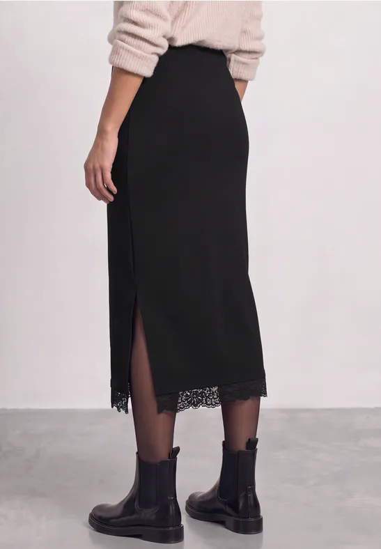 Zwarte midirok met zijsplit en kanten zoom, gecombineerd met zwarte laarzen.
