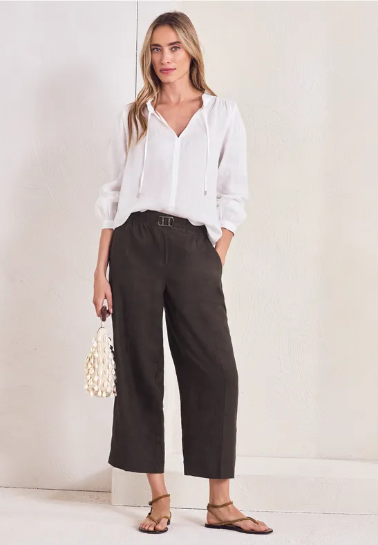 Vrouw in witte blouse, zwarte wijde broek, platte sandalen en klein pareltasje.