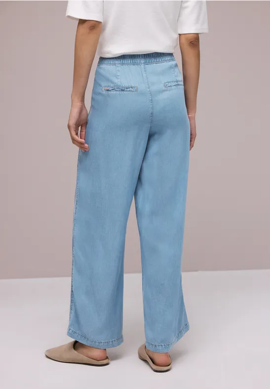 Achteraanzicht van een persoon in wijde lichtblauwe jeans, een witte top en beige sloffen.