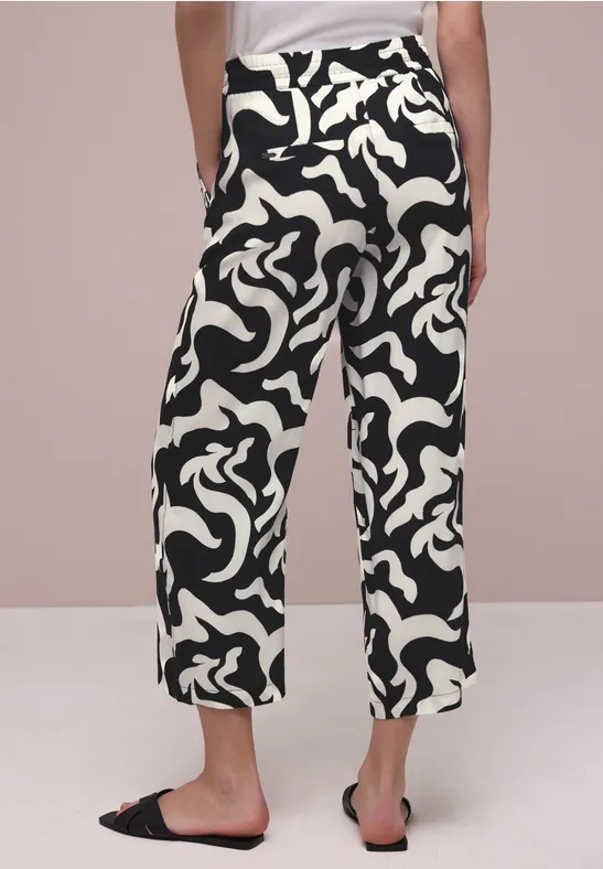 Zwart-witte, wijd gesneden midibroek met abstract patroon, steekzakken, gecombineerd met slippers.