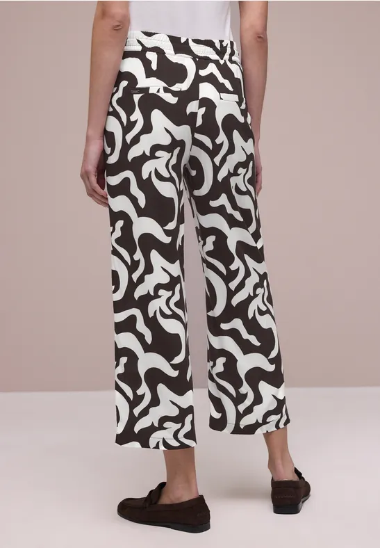 Rückenansicht einer Person mit locker sitzenden Culotte-Hosen in abstraktem Schwarz-Weiß-Muster und schwarzen Hausschuhen.